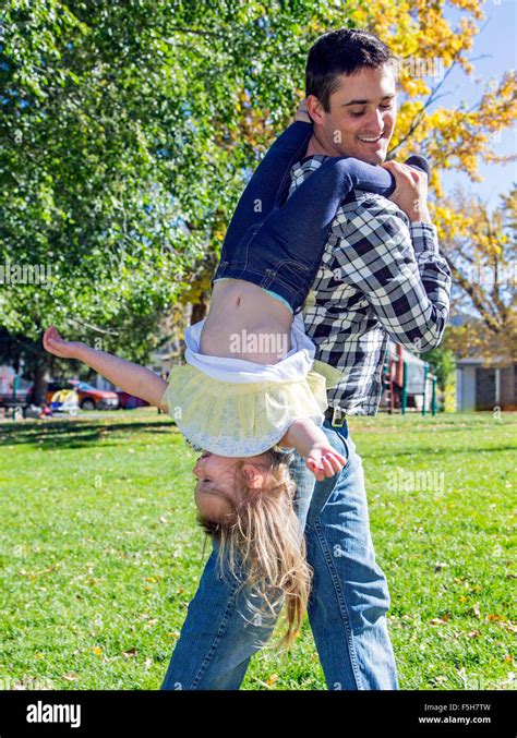 Father Playfully Carrying Young Daughter Upside Down In Park Stock