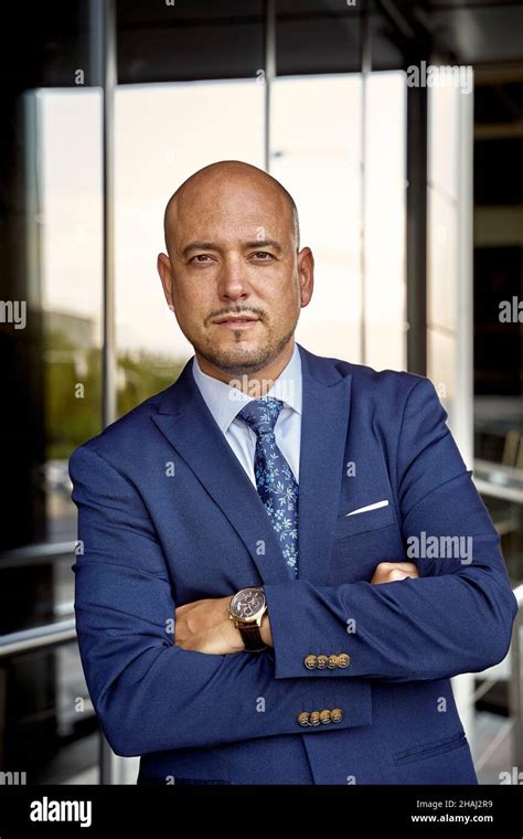 self assured bald businessman crossing arms and looking at camera while standing against glass