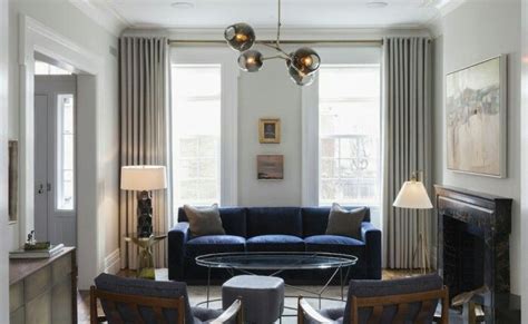 A blue sofa accented with yellow and gray pillows sits on a jute rug at a light wood coffee table seating two white and black stools. Neutral grey tones, royal blue, warm toned accents (With ...