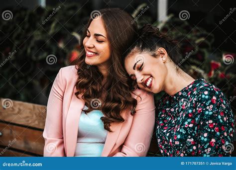 Happy Best Female Friends Enjoying Together Sitting In A Bench