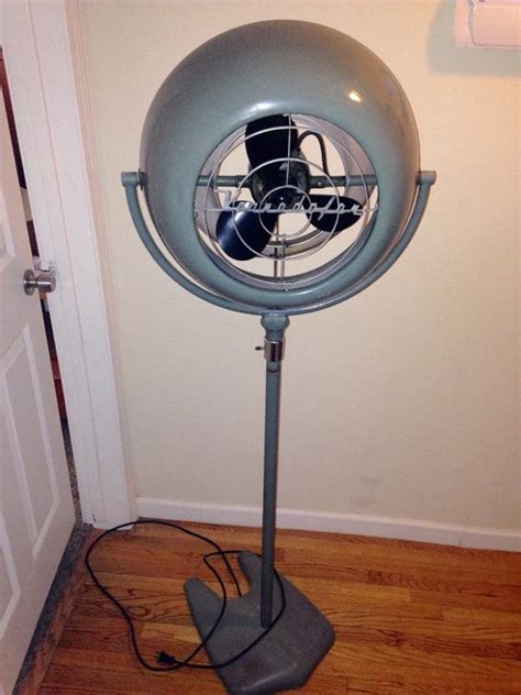 An Old Style Fan Sitting On Top Of A Metal Stand In Front Of A Door