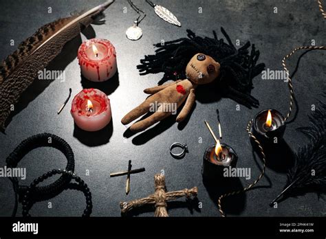 Female Voodoo Doll With Pin In Heart And Ceremonial Items On Grey Table