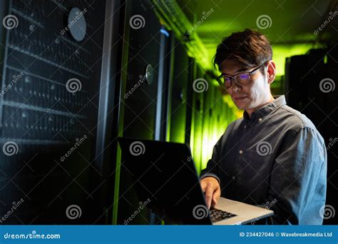 Asian Male Engineer Using Laptop In Computer Server Room Stock Photo