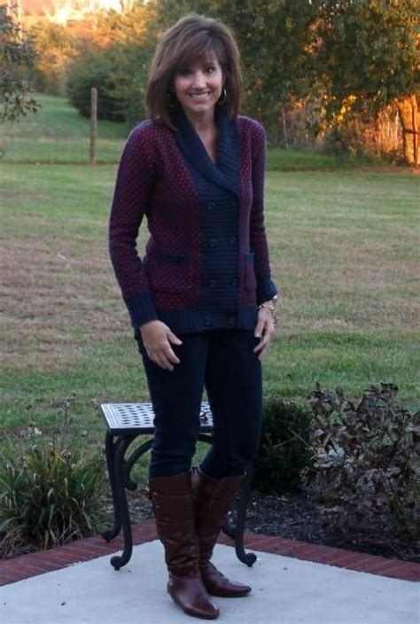 A Woman Standing In Front Of A Park Bench Wearing Boots And A Cardigan Sweater