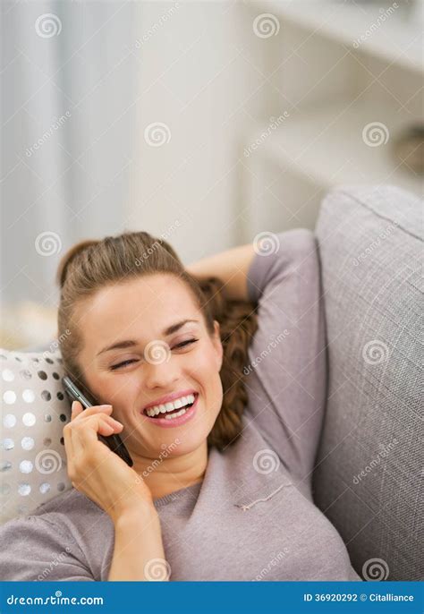 Happy Young Woman Talking Cell Phone While Laying On Sofa Stock Photo