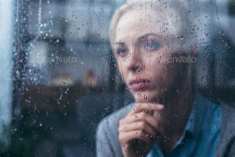 Sad Thoughtful Adult Woman Touching Face At Home Through Window With