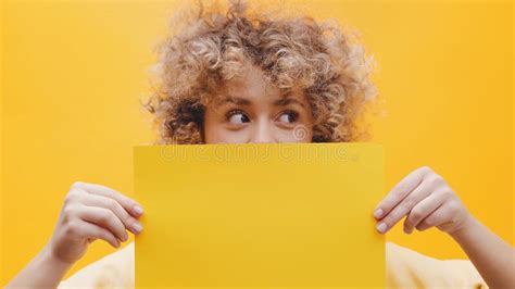 Girl Holding A Yellow Sheet Of Paper Covering Half Of Her Face With The