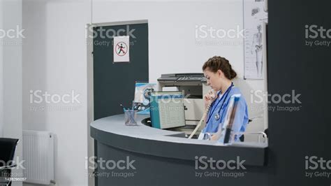 Woman Nurse Answering Landline Phone Call At Reception Desk Stock Photo