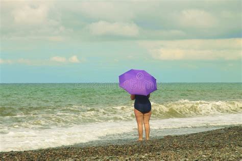 Mature Woman Standing On The Beach Of Sea Shore With Violer Umbrella