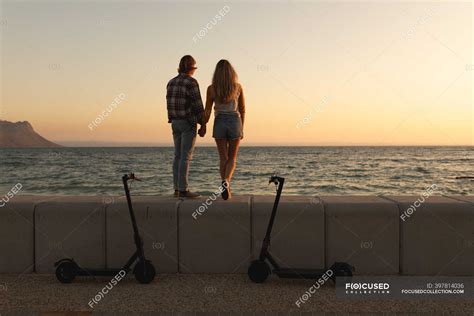 Rear View Of Caucasian Couple Standing On A Promenade By The Sea At