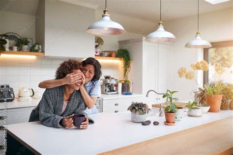 Mature Woman Wearing Pyjamas Surprising Same Sex Partner In Kitchen At Home Together Foto De