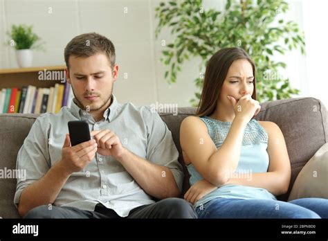 Husband Addicted To Smart Phone Watching Content Beside His Worried Wife Looking Down Sitting On