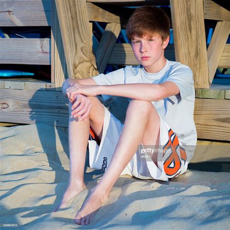 Boy Sitting On Beach Leaning Against Boardwalk High Res Stock Photo