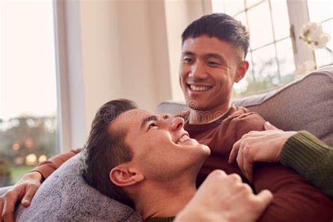 Loving Same Sex Male Couple Cuddling On Sofa At Home Together Stock