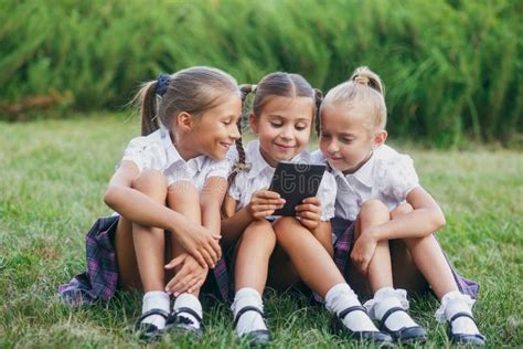Three Little Girls Are Sitting On The Grass And Reading An E Book