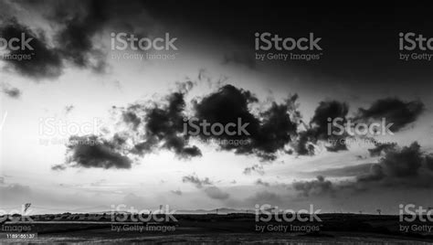 Dark Clouds Over A Green Field At Sunset In Black And White Stock Photo