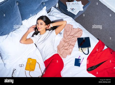 High Angle View Of Attractive Smiling Girl Talking By Smartphone While Lying On Bed With Stylish