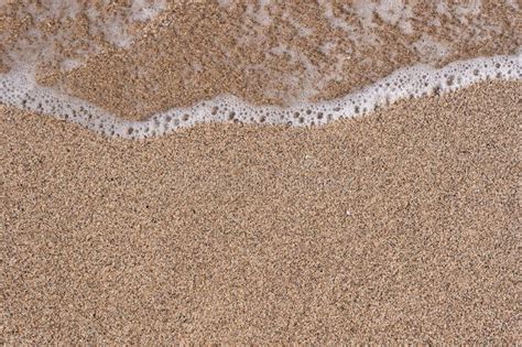 Background Of A Sandy Beach With A Sea Wave Foam From A Wave On The