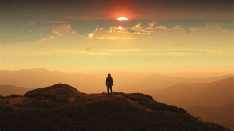 The Man Standing On A Mountain Top Against The Beautiful Sunset Time
