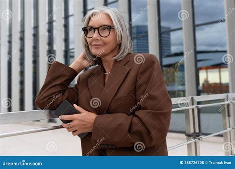 well groomed elderly gray haired business woman in a brown jacket and trousers walks in an urban