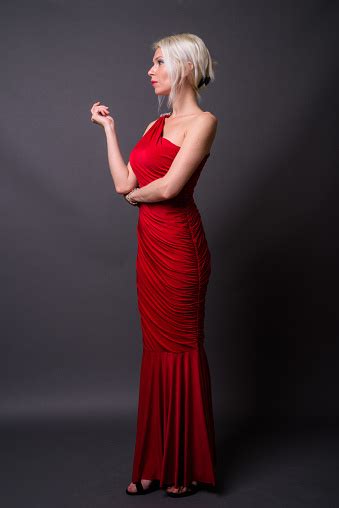 Beautiful Woman With Blond Hair Wearing Red Asymmetric Long Dress Against Gray Background Stock