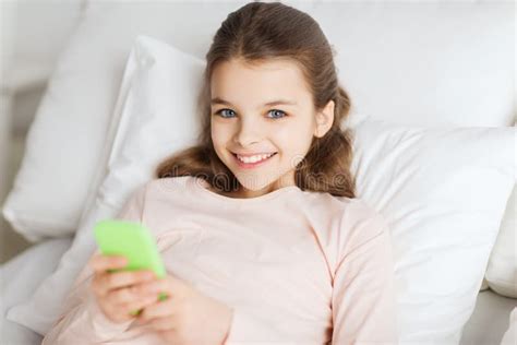 Menina Feliz Que Encontra Se Na Cama Com Smartphone Em Casa Imagem De