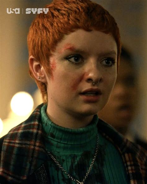 a woman with red hair and piercings wearing a green shirt is looking at
