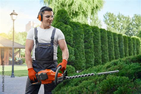 Handsome Caucasian Man In Uniform Safety Glasses And Gloves Using Electric Trimmer For Shaping
