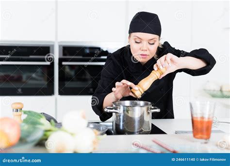 Professional Woman Chef In Black Uniform Peppering Vegetable Soup Stock
