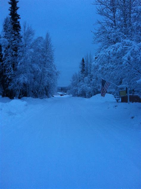 An American Flag Is In The Middle Of A Snow Covered Road With Trees On