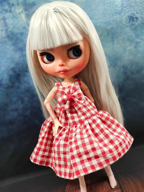 A Doll With White Hair Wearing A Red And White Checkered Dress On Top Of A Wooden Table
