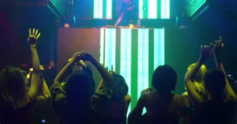 Группа людей танцует в дискотеке в ночном клубе под ритм музыки от диджея на сцене Стоковое