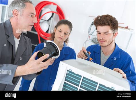 Teacher Observing Students Working On Electrical Appliance Stock Photo