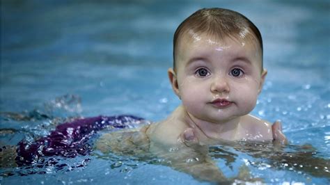 Cute Baby Is Swimming On Body Of Water Wearing Purple