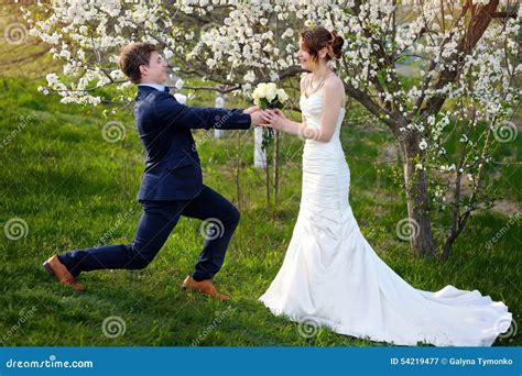 Groom Standing On One Knee And Gives Bride A Wedding Bouquet Stock