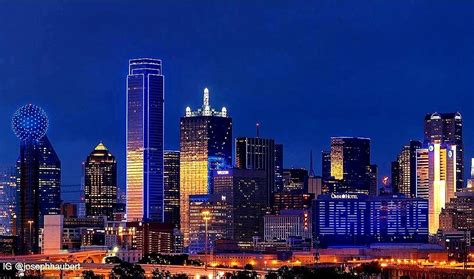 The City Skyline Is Lit Up At Night With Bright Lights And Skyscrapers