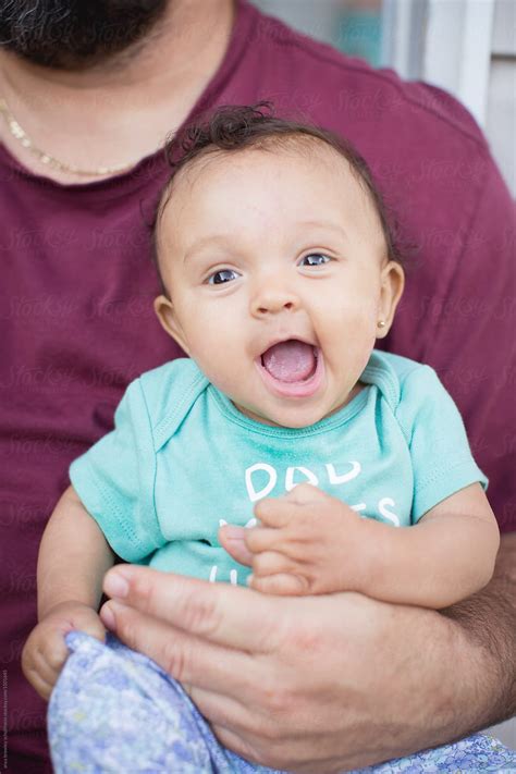 "A Baby Smiling Happily As She Is Held By Her Father" by Stocksy