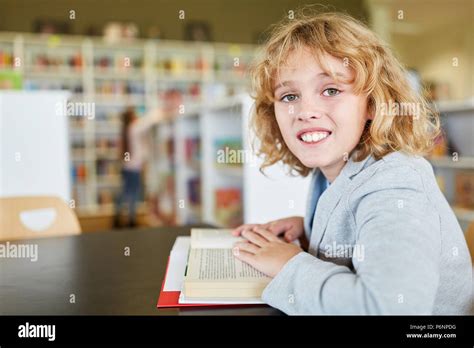 Happy Blond Boy Is Reading In A Book In The Library Of Elementary