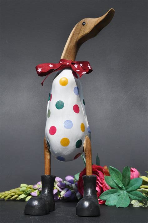 A Wooden Duck With Polka Dots On Its Head And Boots Next To Flowers