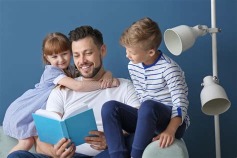 Father And His Children Reading Book Together At Home Stock Photo