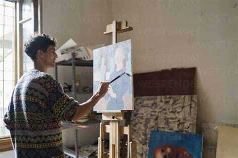 Male Artist Painting Canvas At Easel In Artists Studio Stock Photo