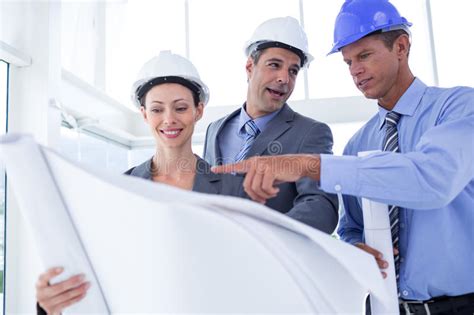 Businessmen And A Woman With Hard Hats And Holding Blueprint Stock