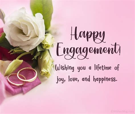 Wedding Rings And Flowers On Pink Background With Happy Engagement