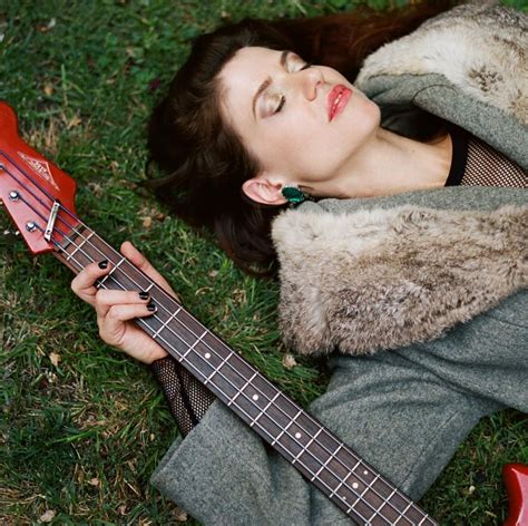 A Woman Laying On The Grass With A Guitar In Her Hand And Eyes Closed
