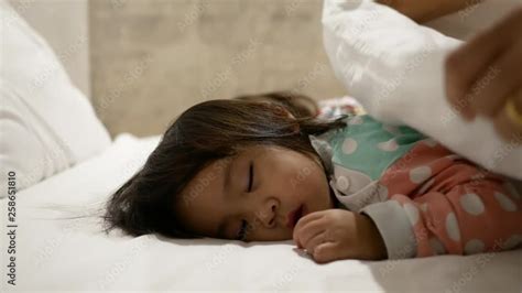 asian mother is putting blanket on her daughter who is sleeping in the bed and goodnight kiss