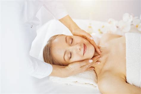 Beautiful Caucasian Woman Enjoying Facial Massage With Closed Eyes In Sunny Spa Salon Relaxing