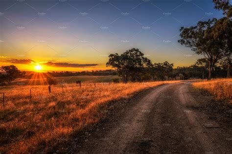 Countryside Landscape With Rural Dirt Road At Sunset In