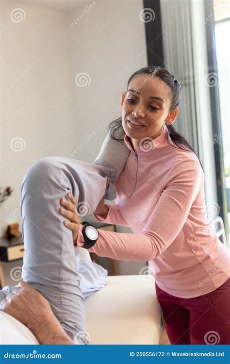 Biracial Female Physiotherapist Giving Leg Massage Therapy To Caucasian Senior Man At Home Stock