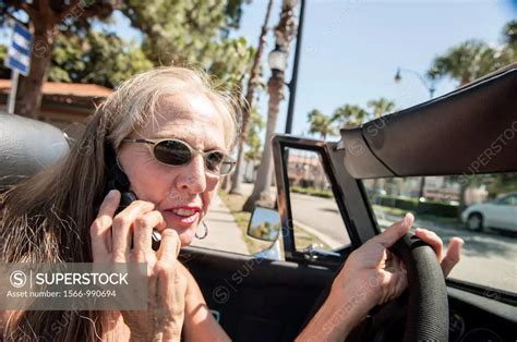 57 Year Old Woman With Long Hair Driving Her Mg Convertible Car And Talking On A Cell Phone