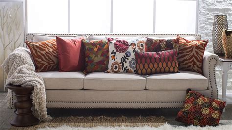 A Couch With Many Pillows On Top Of It In Front Of A White Wall And Windows